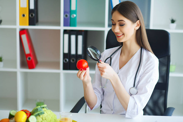 Zdraví. Doktor podepíše dietní plán. Dietolog drží v hrsti čerstvých rajčat. Ovoce a zelenina. Mladý doktor s milým úsměvem v kanceláři. Vysoké rozlišení - Fotografie, Obrázek