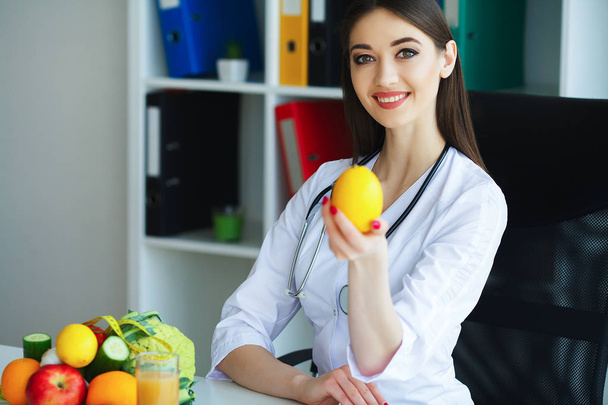 Salud. El doctor dietista sonríe y muestra a Lemon. Mujer sostiene fruta en las manos. Joven Doctor con una hermosa sonrisa en la oficina de la luz. Alta resolución
 - Foto, imagen