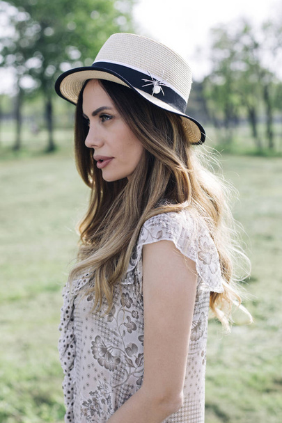 Portrait of a beautiful elegant woman with hat posing in the park at sunny summer day - Foto, Imagen