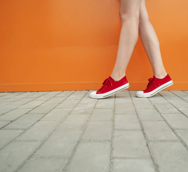 Κοπέλα φορώντας trendy κόκκινα παπούτσια. Παπούτσια με κοντινό σουτ μπροστά από πορτοκαλί τοίχο για κατάστημα μόδας - Φωτογραφία, εικόνα