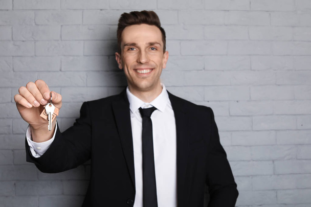 Male real estate agent with key on brick wall background - Foto, afbeelding