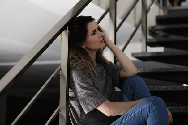 Lonely depressed woman sitting on stairs indoors - Фото, зображення