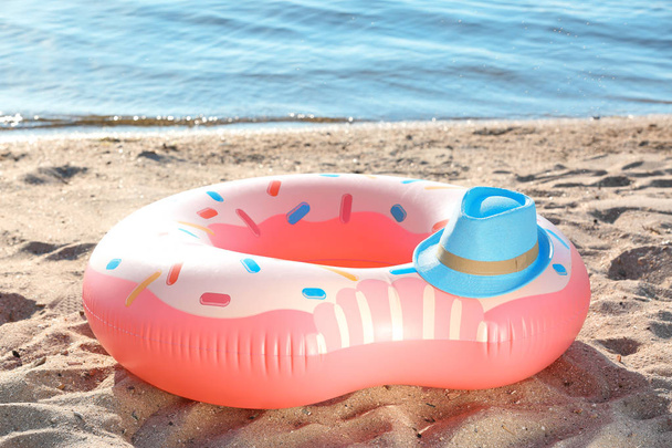 Inflatable donut and hat on sand near sea. Beach object - Fotoğraf, Görsel