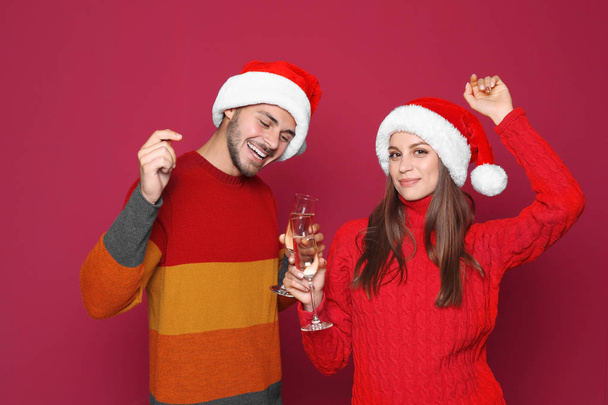 Young couple in Santa hats with glasses of champagne on color background. Christmas celebration - Foto, immagini