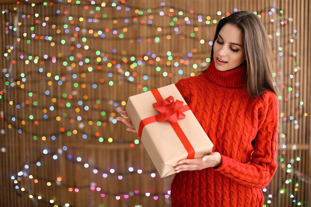 Beautiful young woman with Christmas gift on blurred lights background - Φωτογραφία, εικόνα