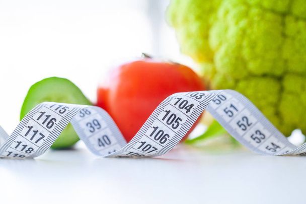 Diet. Fitness and healthy food diet concept. Balanced diet with vegetables. Fresh green vegetables, measuring tape on white background. Closeup - Photo, Image