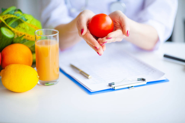 Ernährung. Ernährungsmedizinerin hält Tomate in ihrem Büro. Konzept natürlicher Ernährung und gesunder Lebensweise. Fitness und gesunde Ernährung. Ausgewogene Ernährung mit Gemüse. - Foto, Bild
