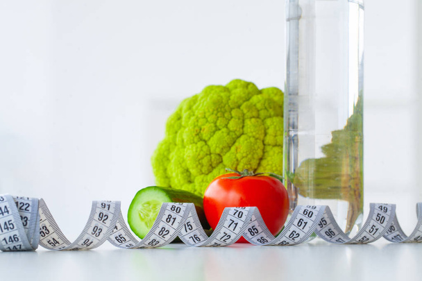 Диета. Концепция здорового питания. Сбалансированная диета с овощами. Свежие зеленые овощи, измерительная лента на белом фоне. Крупный план
 - Фото, изображение