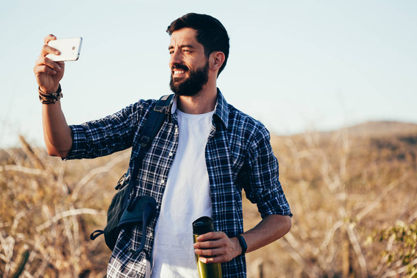Man with backpack taking selfie with his mobile phone during desert hike - Foto, Bild