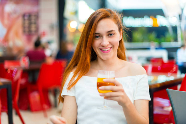 Νέοι κοκκινομάλλα όμορφη κοπέλα απολαμβάνοντας μια μπύρα σε ένα εμπορικό κέντρο - Φωτογραφία, εικόνα