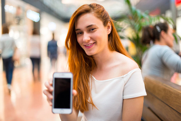 Ruda młoda Ładna dziewczyna w centrum handlowym, prowadzenie rozmowy z telefonu komórkowego z kimś - Zdjęcie, obraz