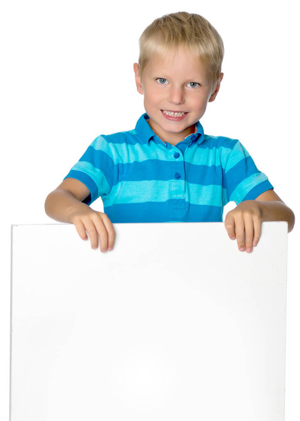 Ένα μικρό αγόρι ψάχνει από πίσω από ένα άδειο πανό. - Φωτογραφία, εικόνα