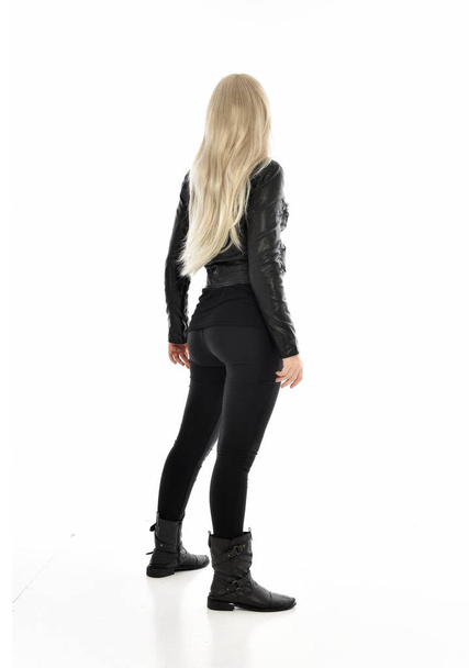 Ganzkörperporträt eines blonden Mädchens in schwarzer Lederkleidung. stehend mit dem Rücken zur Kamera posieren. isoliert auf weißem Studiohintergrund. - Foto, Bild