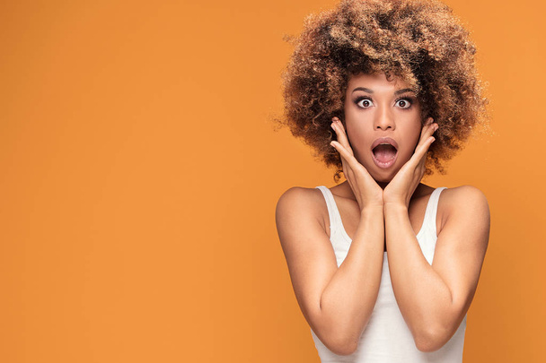 Surprised amazed beautiful afro woman with wide open mouth looking at camera. Shocked girl posing on yellow background. - Φωτογραφία, εικόνα