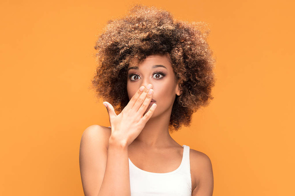 Surprised amazed beautiful afro woman looking at camera. Girl posing on yellow background. - Foto, immagini