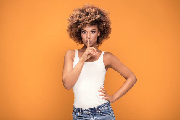 Young afro woman keeping index finger on mouth, yellow background. - Fotoğraf, Görsel