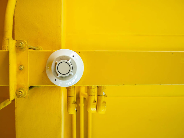 Білий дзвінок пожежної сигналізації, прикріплений на жовтій стелі
. - Фото, зображення
