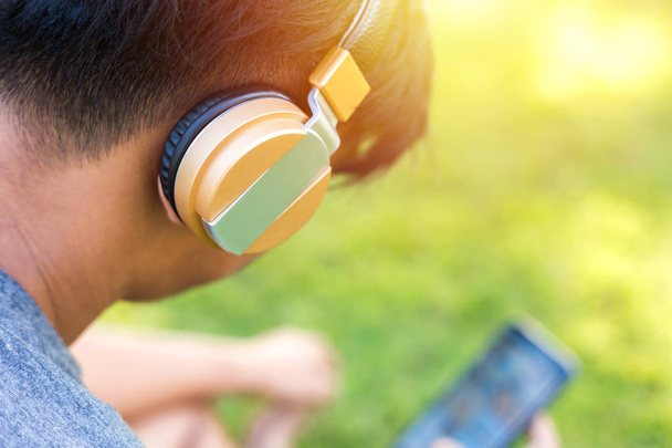 A Man wear headphone and play phone. He sitting on the green grass. - 写真・画像