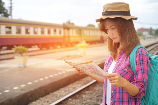 バックパックと鉄道駅、旅行、旅行の概念に計画の地図を探して帽子と若い女性旅行者 - 写真・画像