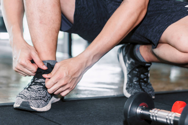 Mann bindet ihre Schnürsenkel mit Fitnessgeräten im Fitnessstudio - Foto, Bild