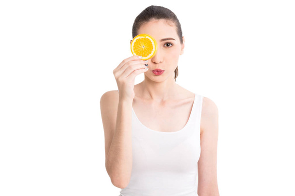 Beautiful woman holding orange slice hiding eye behind isolated on white background - 写真・画像