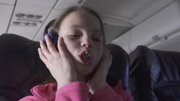 Cheerful teenage girl listens to music on headphones in the cabin of plane while traveling stock footage video - Záběry, video
