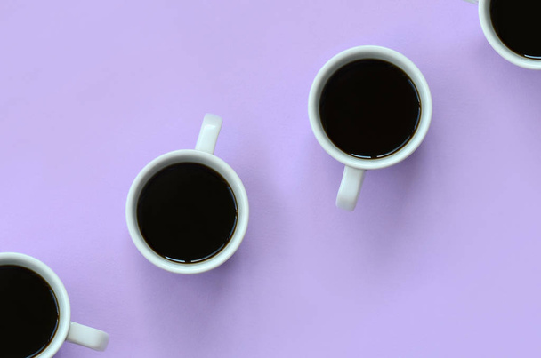 Многие маленькие белые чашки кофе на фоне текстуры моды пастельно-фиолетовой цветной бумаги в минимальной концепции
. - Фото, изображение