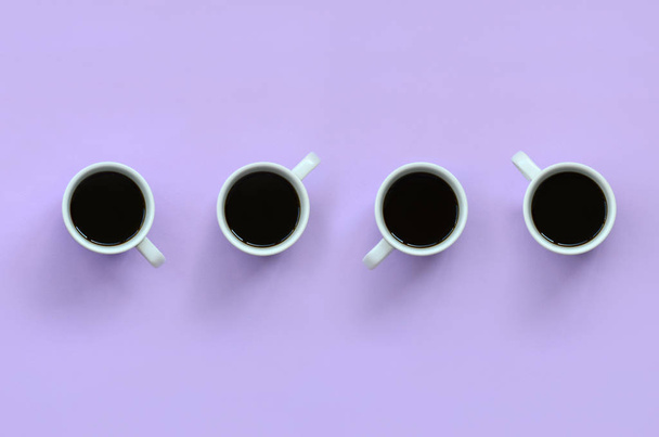 Многие маленькие белые чашки кофе на фоне текстуры моды пастельно-фиолетовой цветной бумаги в минимальной концепции
. - Фото, изображение