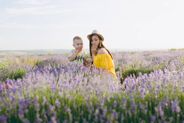 Young woman in yellow dress walk on purple lavender flower meadow field background, rest, have fun, play with little cute child baby boy. Mother, small kid son. Family day, parents, children concept - Photo, Image