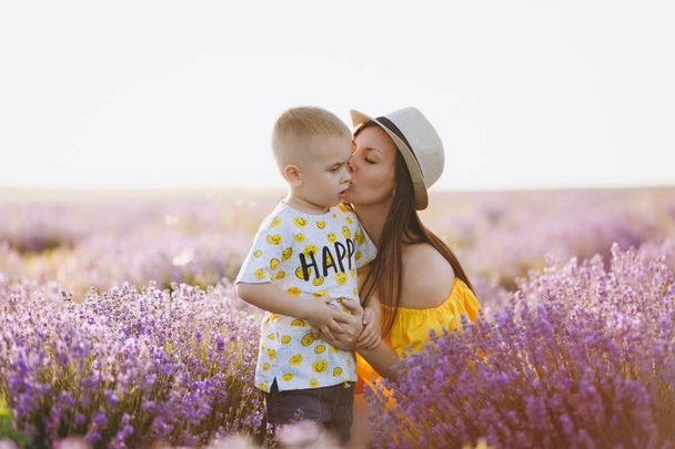 Fiatal nő a sárga ruha járni a levendula lila virág meadow mező háttér, pihenés, szórakozni, játszani a kis aranyos gyerek baba fiú. Anya, a kis gyerek fia. Családi nap, szülők, gyermekek koncepció - Fotó, kép