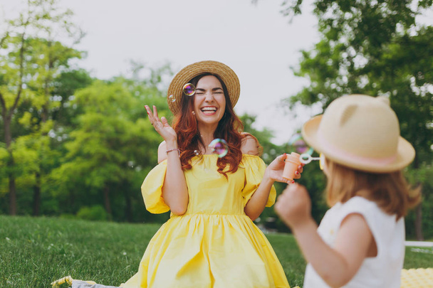 lachende Frau in gelben Kleidern spielen im Park Spaß haben, amüsieren mit kleinen niedlichen Kind Baby Mädchen halten Seifenblasengebläse. Mutter, kleine Tochter. Muttertag, Liebe Familie, Elternschaft, Kindheit - Foto, Bild