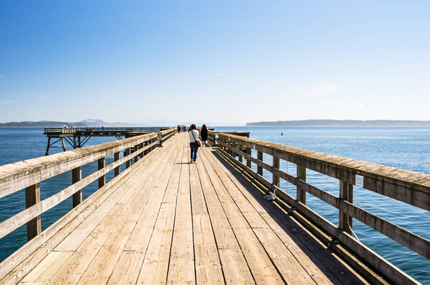 Mensen lopen op een houten Pier op een heldere dag van de zomer - Foto, afbeelding