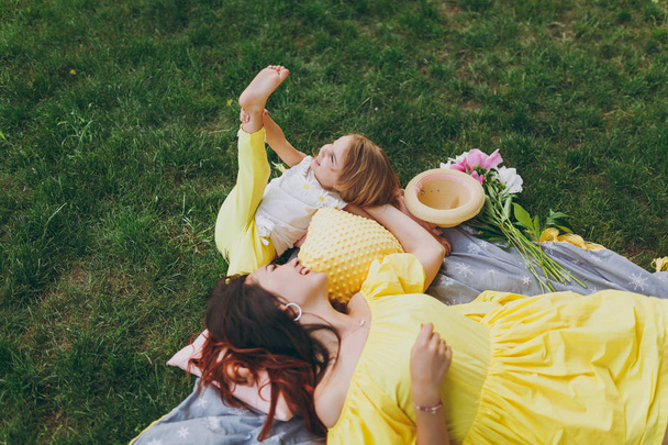 Iloinen nainen keltainen mekko makaa vihreä ruoho nurmikko puistossa pelata ja levätä, pitää hauskaa pieni söpö lapsi vauva tyttö. Äiti, pieni tytär. Äitienpäivä, rakkausperhe, vanhemmuus, lapsuus
 - Valokuva, kuva