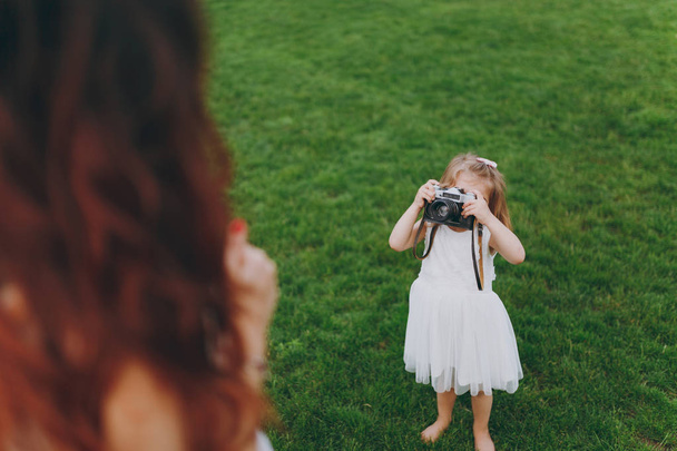 Malé dítě holčičku v lehké šaty vyfotit maminka na retro vinobraní fotoaparát na zelené trávě v parku. Matka, dítě dceruška. Den matek, láska rodina, rodičovství, dětství koncept - Fotografie, Obrázek
