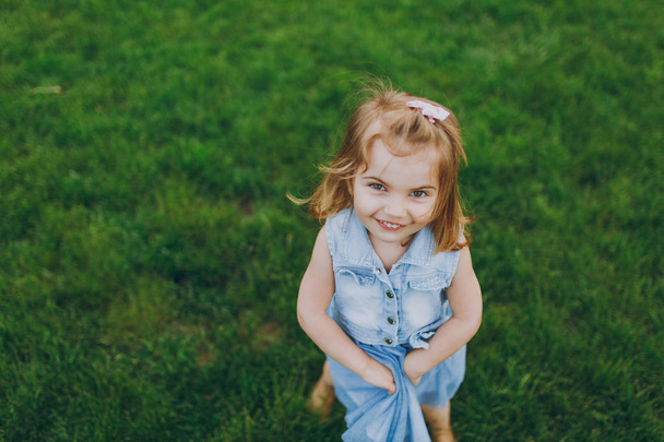 Smiling little cute child girl in denim dress looking up and have fun on green grass lawn in park. Мама, маленькая дочка. Mother 's Day, love family, parenthood, childhood concept
 - Фото, изображение