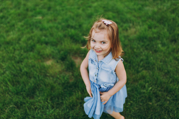 Pretty little cute child baby girl in denim dress looking up and have fun on green grass lawn in park. Mother, little kid daughter. Mother's Day, love family, parenthood, childhood concept - Fotografie, Obrázek