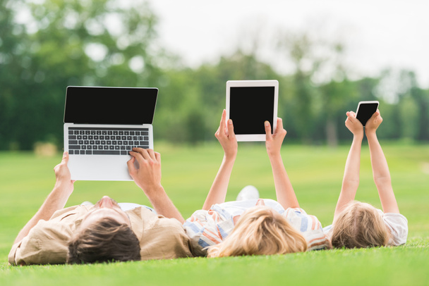 famille couché sur l'herbe et en utilisant des appareils numériques avec des écrans vides
 - Photo, image