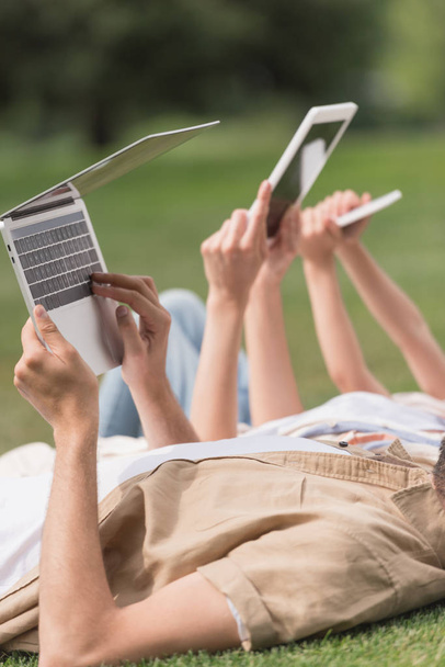 cropped shot of family using digital devices while lying on lawn in park - Fotografie, Obrázek