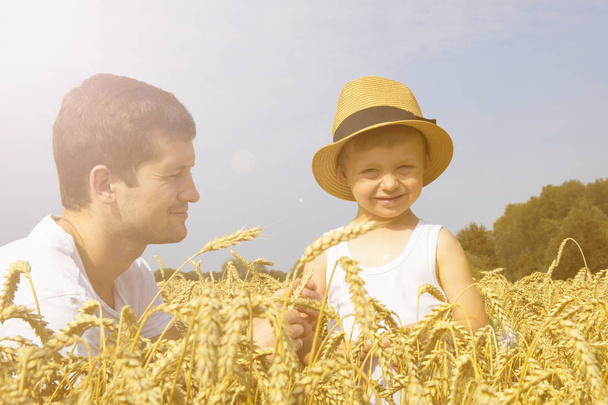 Happy family. Father and son on the wheat field. Male shows the boy ear of wheat. - Foto, Imagem