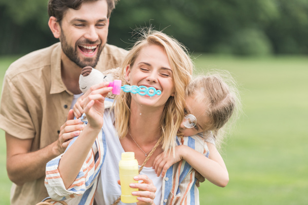 happy family with one child hugging and blowing soap bubbles in park  - Foto, immagini