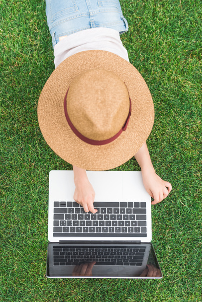 overhead view of child in hat using laptop on green lawn - 写真・画像