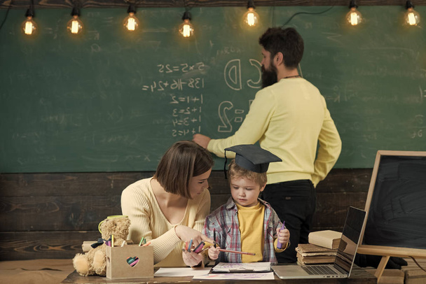 alternative study. Mother teaches clever son, while father writes on chalkboard on background. Boy listening to mom with attention. Homeschooling concept. - Photo, Image