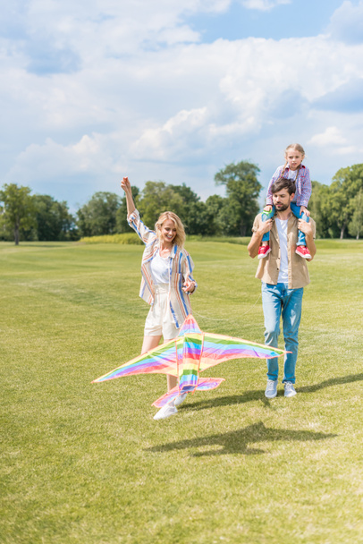 ευτυχείς και νέοι γονείς και χαριτωμένη μικρή κόρη παίζει με πολύχρωμα χαρταετού στο πάρκο  - Φωτογραφία, εικόνα