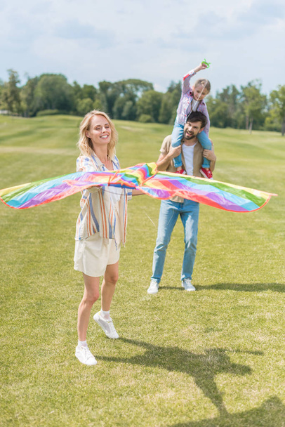 happy parents with cute little daughter playing with colorful kite in park  - Zdjęcie, obraz