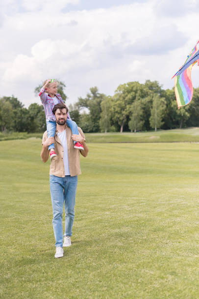 счастливый отец с маленькой дочерью, играющей с цветным воздушным змеем в парке
 - Фото, изображение
