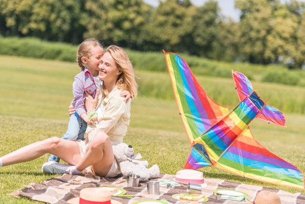happy mother and daughter hugging while sitting on plaid at picnic - Фото, изображение