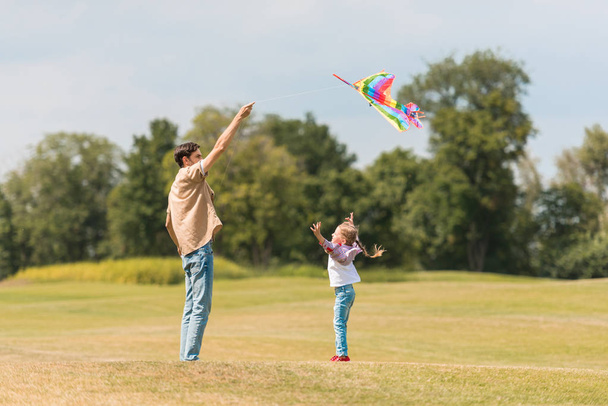 vue latérale de père heureux et petite fille jouant avec cerf-volant coloré dans le parc
 - Photo, image