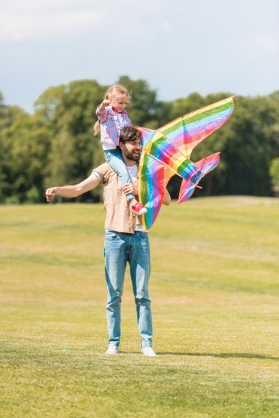 happy father carrying little daughter on neck and playing with colorful kite in park  - Foto, immagini