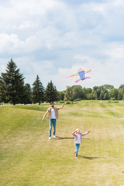 happy father and daughter playing with kite and running on lawn in park - Foto, Imagen