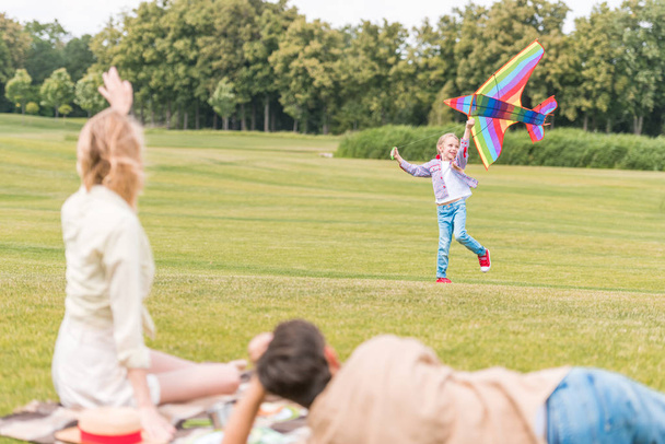 selective focus of parents looking at daughter playing with kite in park - Foto, imagen